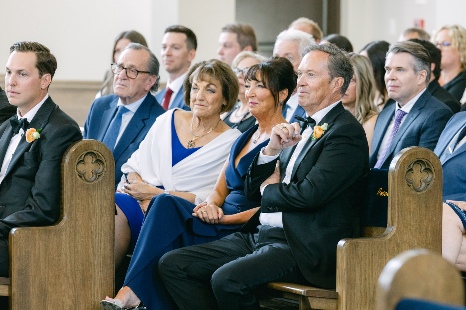 A group of well-dressed people seated in church pews during a formal event, attentively looking forward