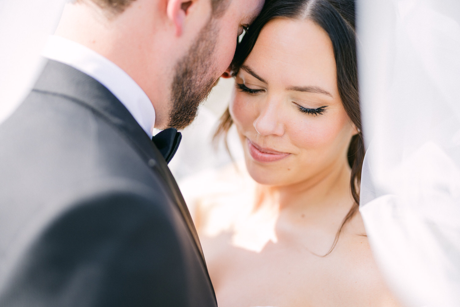 A close-up shot of a bride and groom sharing a tender moment, faces close together with the bride's eyes gently closed.