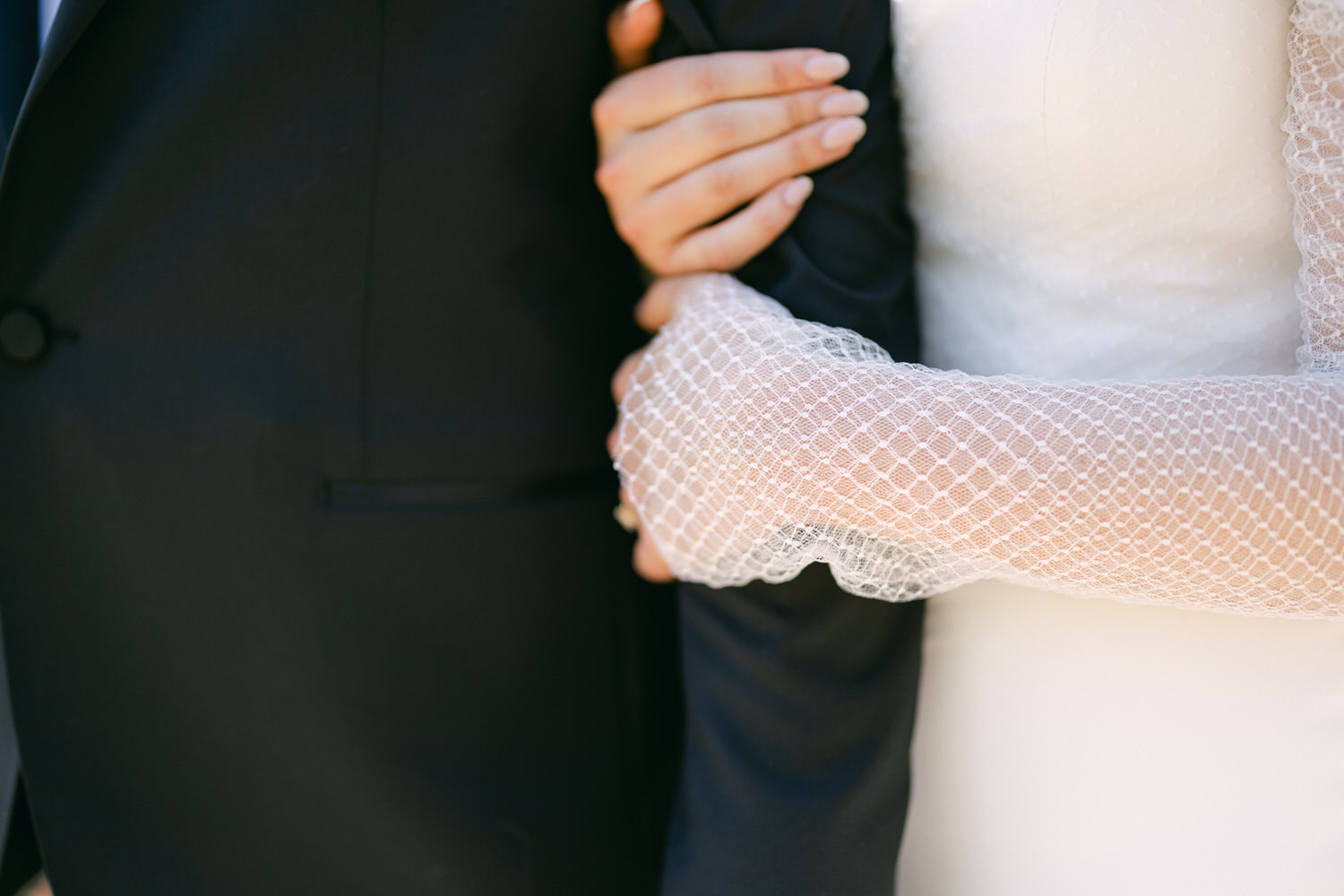 Close-up of bride and groom holding hands, showcasing wedding attire and lace details