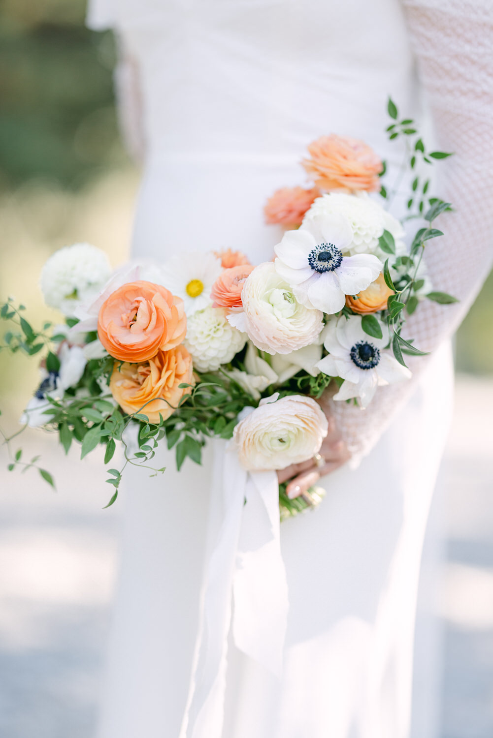 A close-up photo of a bride holding a beautiful wedding bouquet with white, peach, and blue flowers.