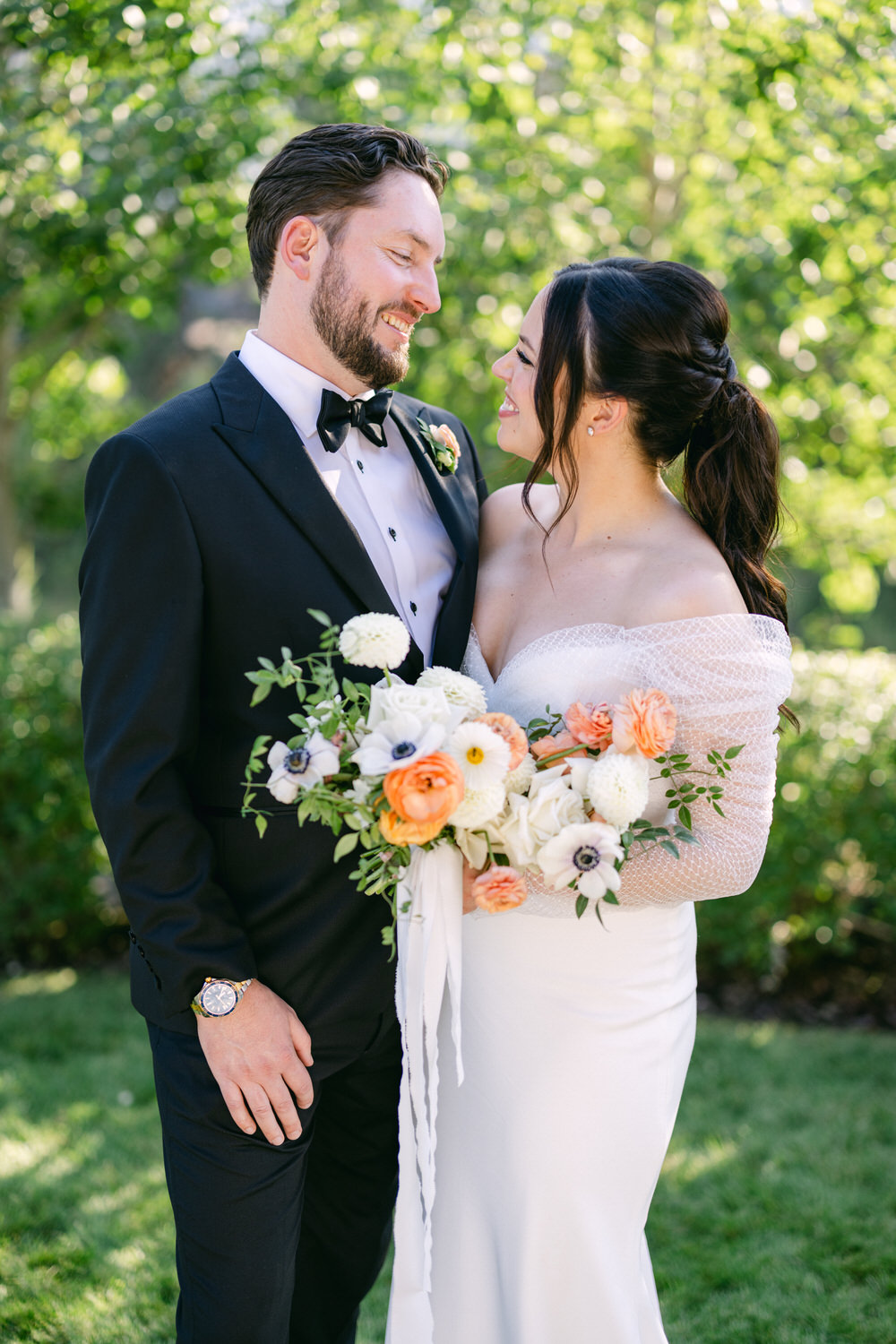 A smiling couple in wedding attire looking at each other affectionately, with the bride holding a bouquet of flowers.