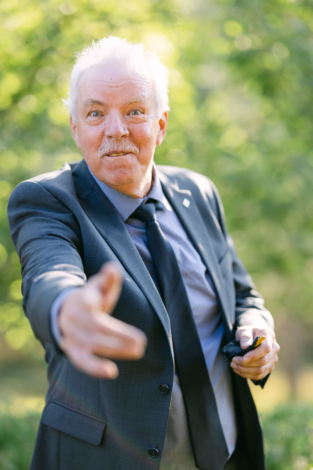 A senior man with a friendly expression extending his hand for a handshake outdoors with a blurred green background