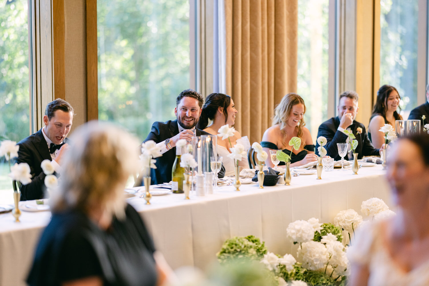 Guests laughing and conversing at a wedding reception table adorned with white flowers.