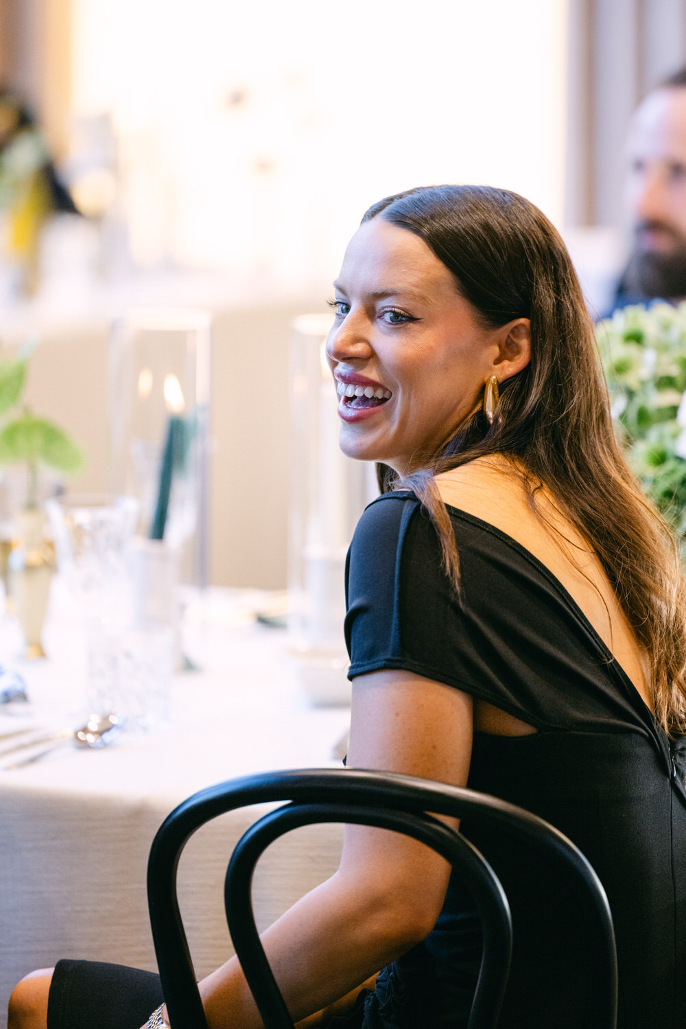 Woman in a black dress laughing while sitting at a decorated table during a social gathering