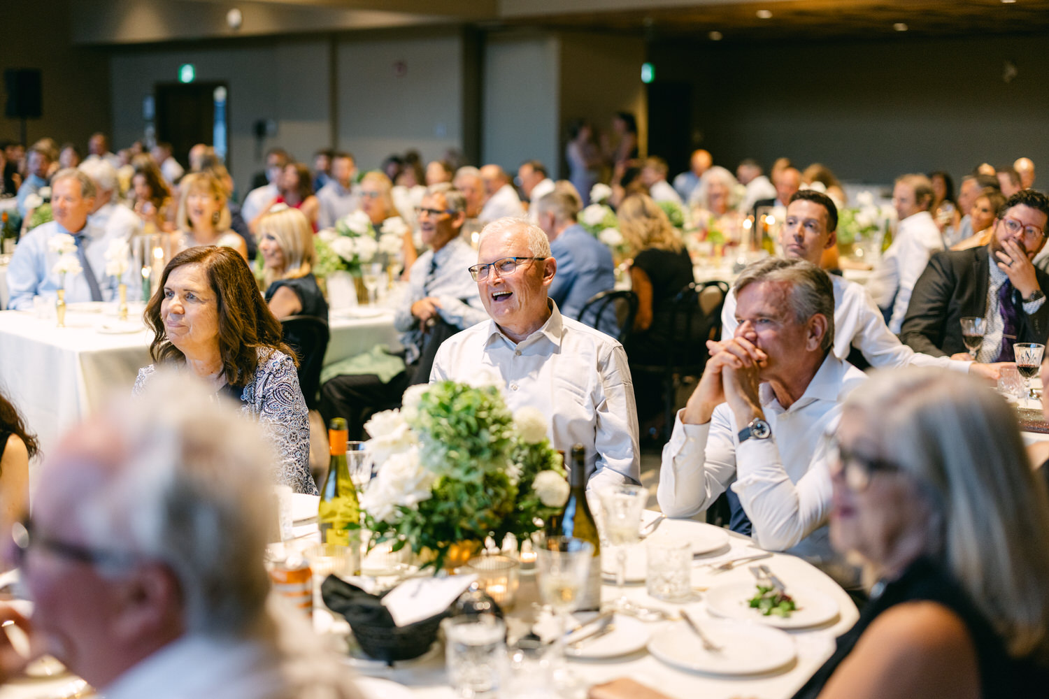 A group of people laughing and enjoying an event at a banquet with tables decorated with flowers and candles.