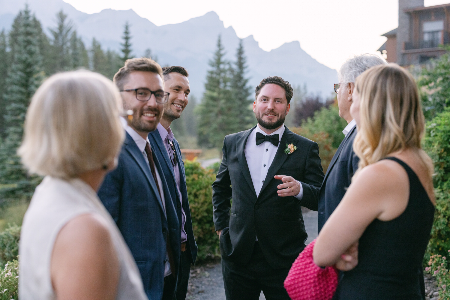 Group of people conversing outdoors with mountains in the background during a wedding event.