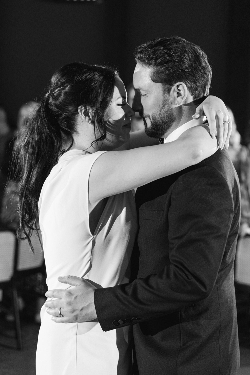 A black and white photo of a bride and groom sharing a close dance, looking into each other's eyes with affection.