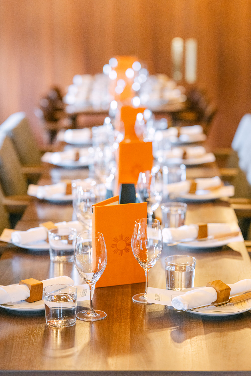 A well-arranged dining table with wine glasses, water glasses, folded napkins, and menu cards in a warm, cozy restaurant interior.