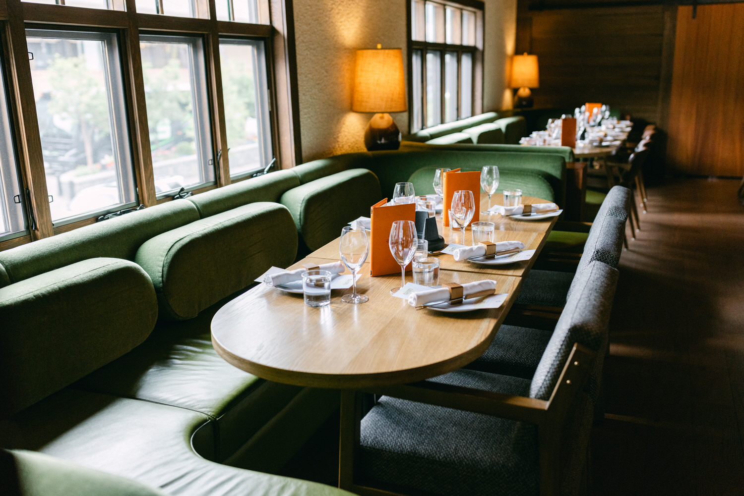 An upscale dining room with neatly arranged tables, green upholstered seating, and warm lighting.