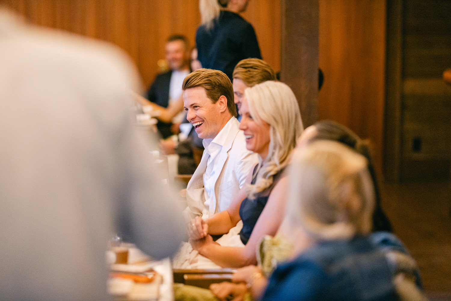 People smiling and looking engaged at an event, as they listen to someone speaking off-camera.