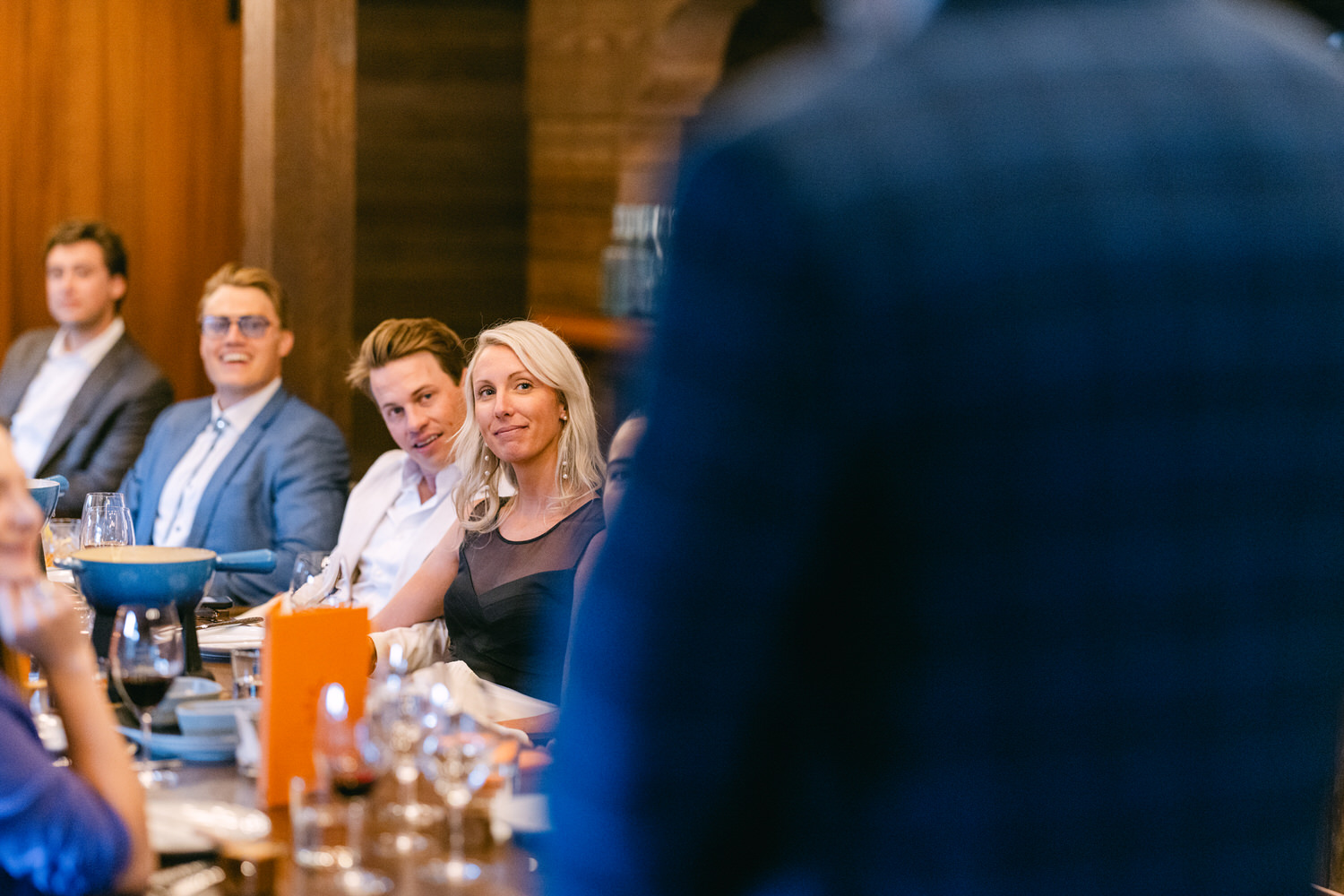 Group of professionals seated at a dinner table engaging in conversation with focus on a woman in the foreground