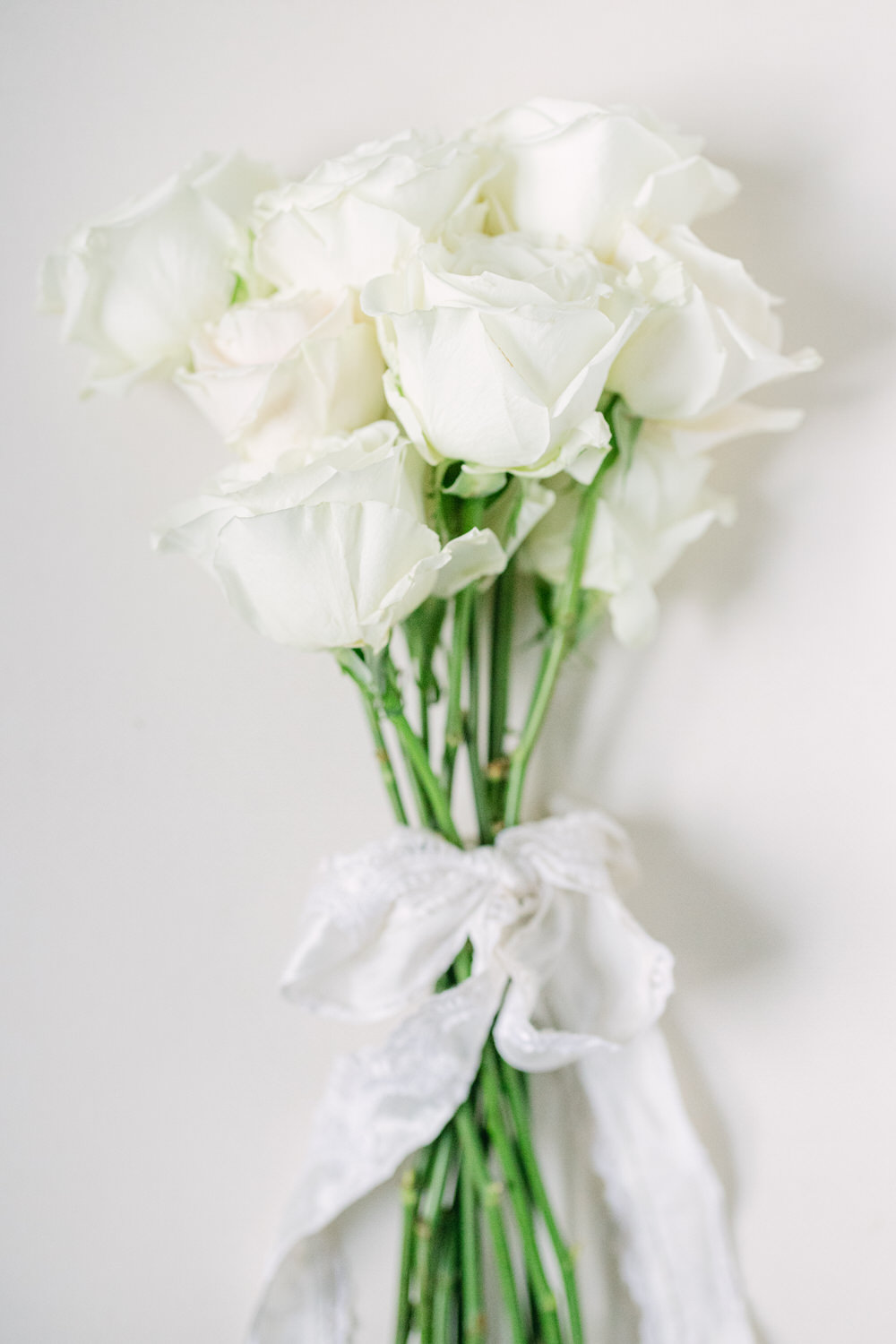 Bunch of white roses tied with a white ribbon against a light background.