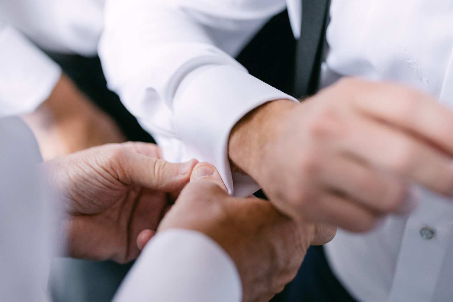 Close-up of hands assisting in fastening cufflinks on a white dress shirt