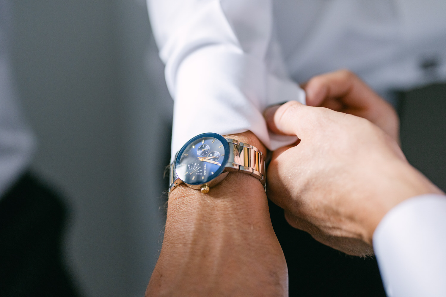 Close-up of a person's hand adjusting a stylish wristwatch with a blue face and metallic strap.