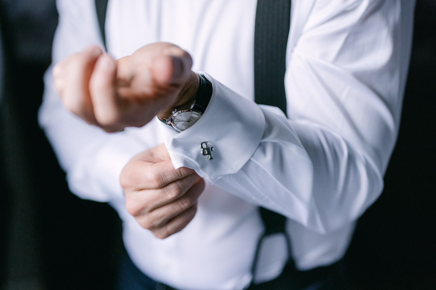 Close-up of a man's hands adjusting his cufflinks with a crisp white shirt and wristwatch visible