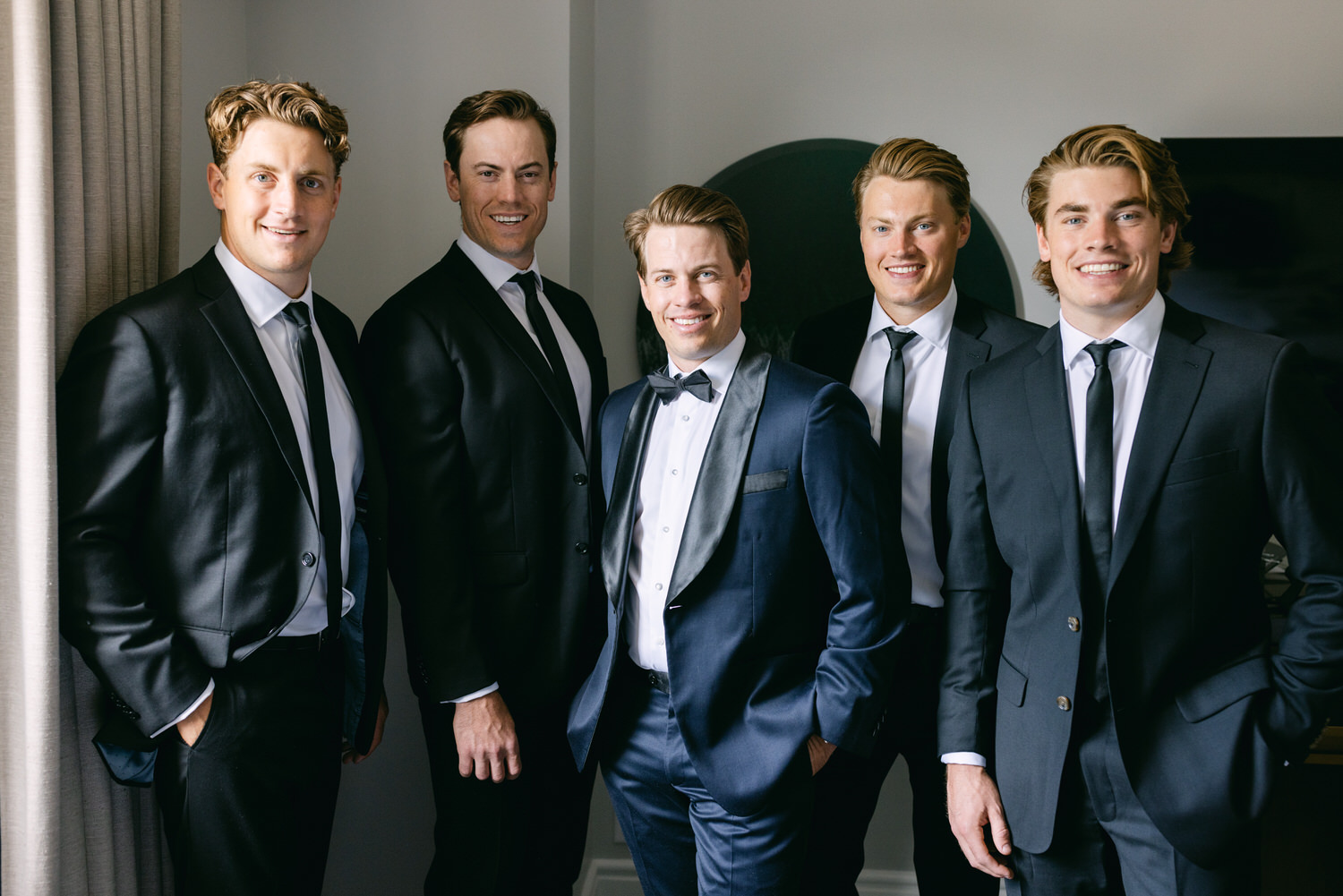 Five men dressed in formal suits smiling confidently at a formal event.