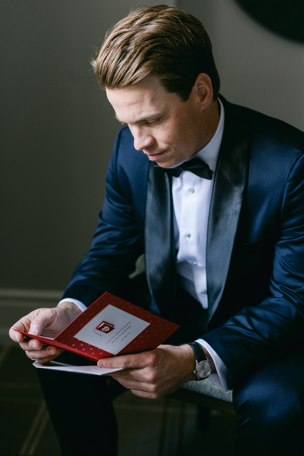 A man in a formal suit and bowtie attentively reading a card.