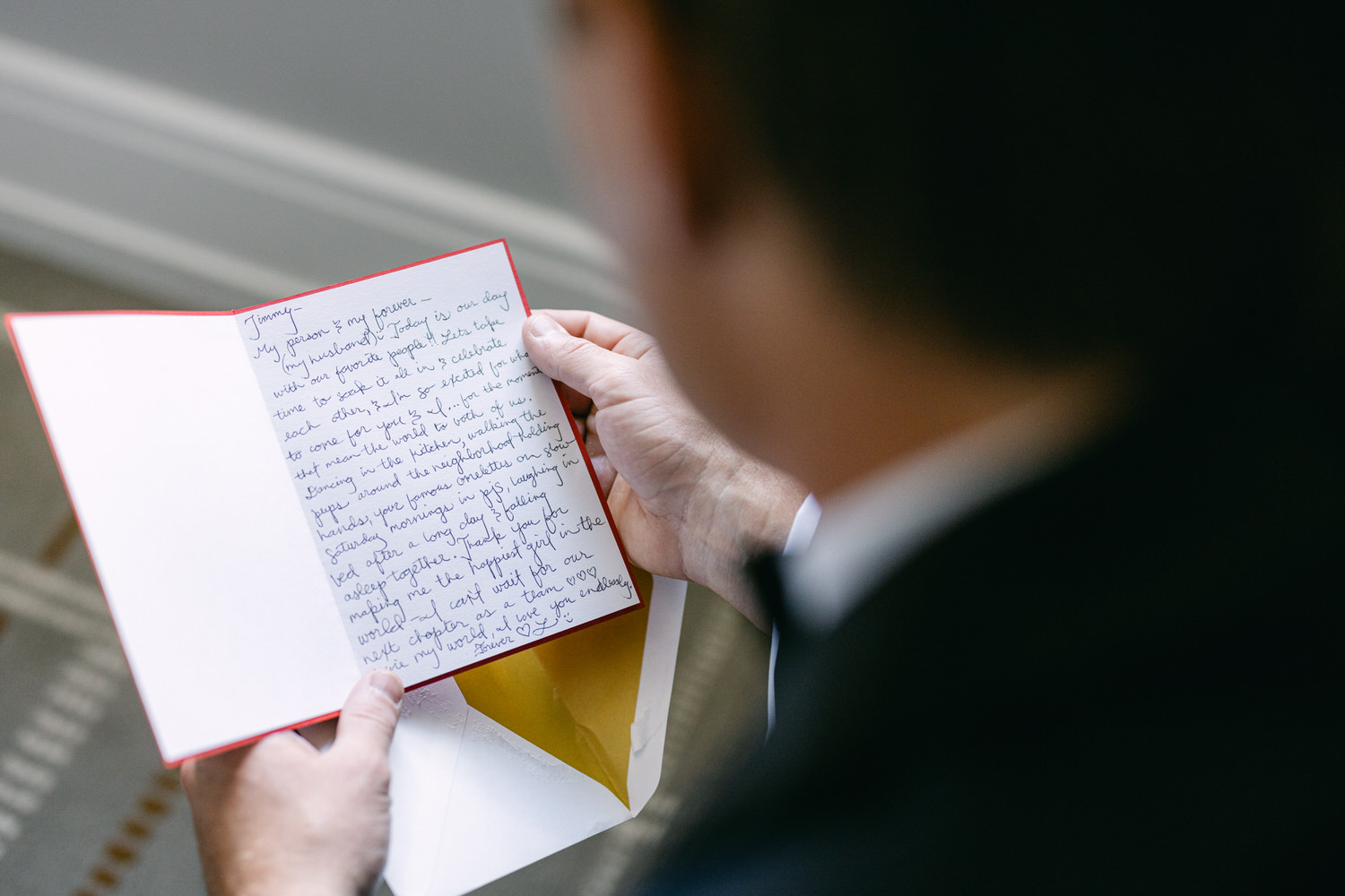 Over-the-shoulder view of a man in a suit reading a handwritten letter with red ink.