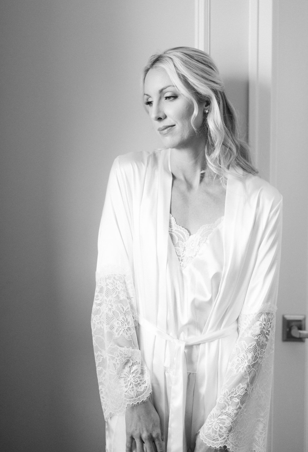 A black and white photo of a woman gazing away thoughtfully, dressed in a silky robe with lace details.