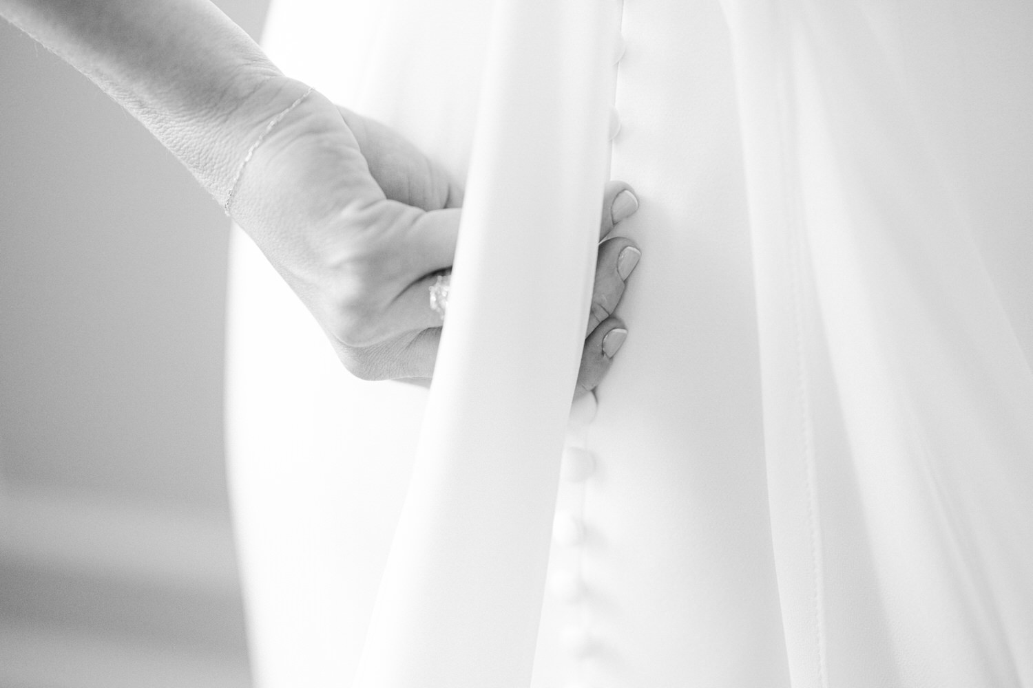 Close-up view of a hand fastening the buttons on the back of a white bridal gown