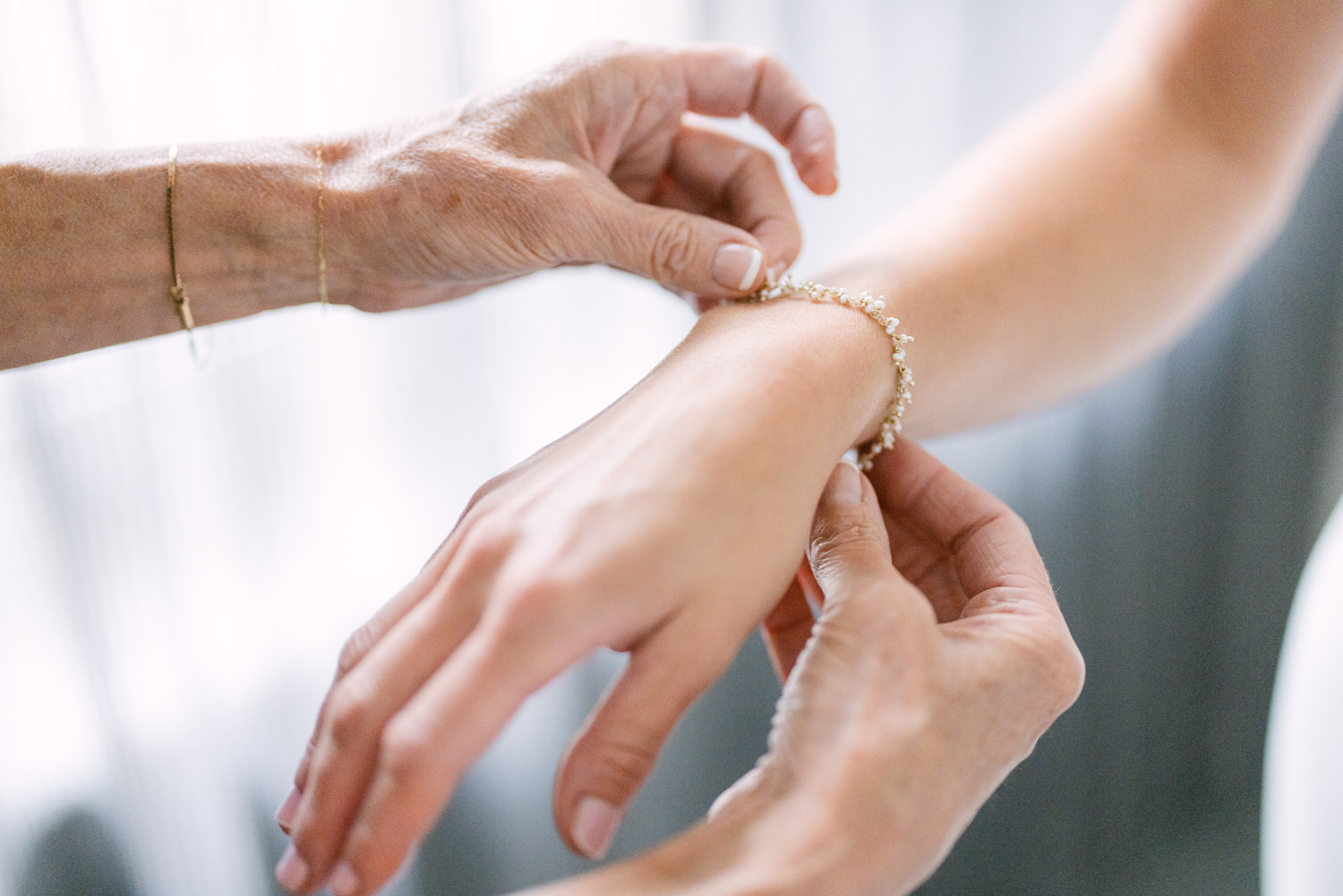 An elderly person fastens a bracelet on a younger person's wrist, symbolizing a connection between generations.