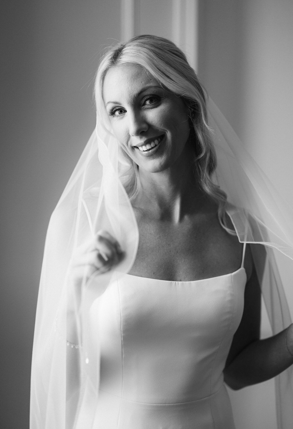 A black and white portrait of a smiling bride in her wedding dress and veil.