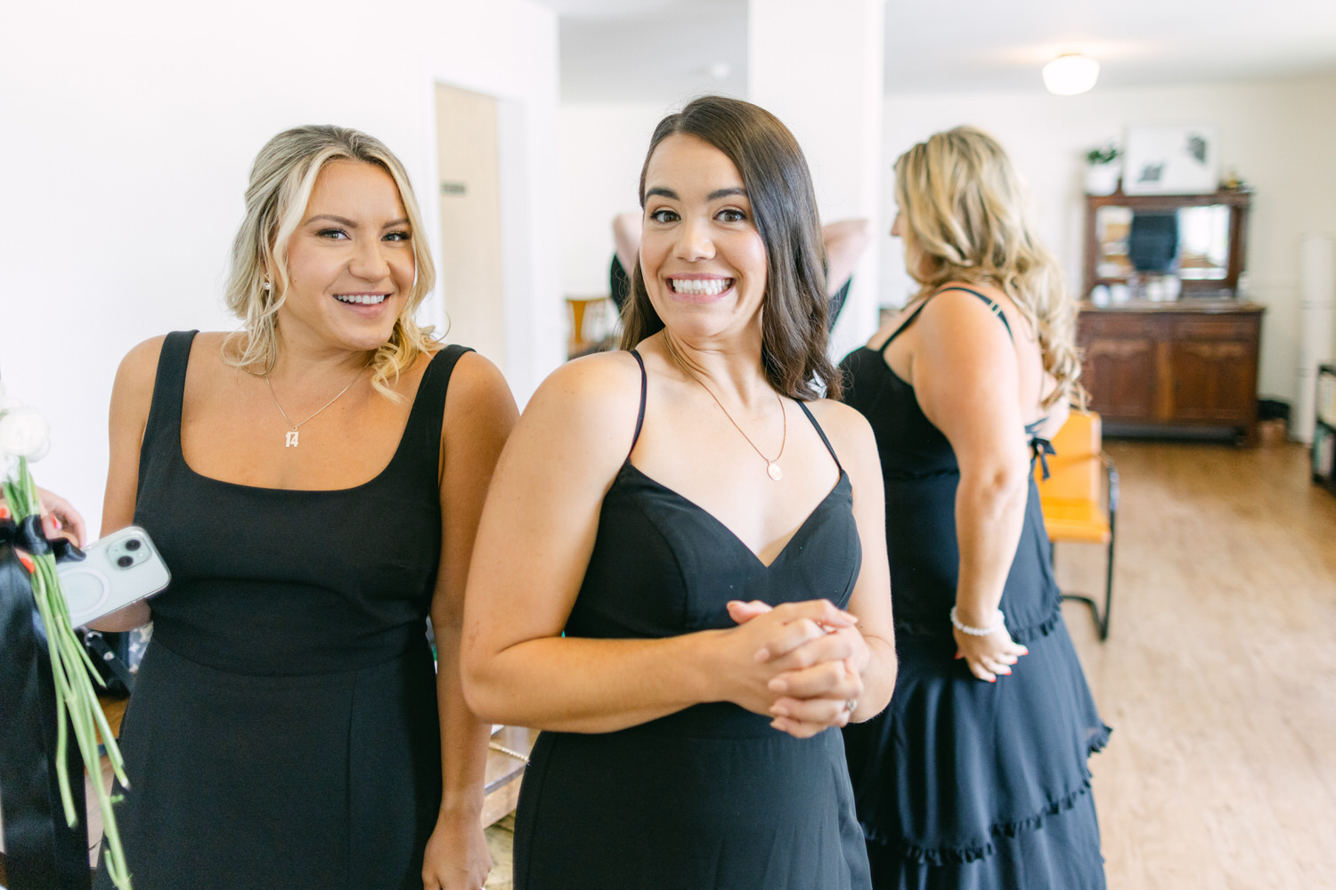 Two smiling bridesmaids in black dresses standing in a room with elegant interior decor.