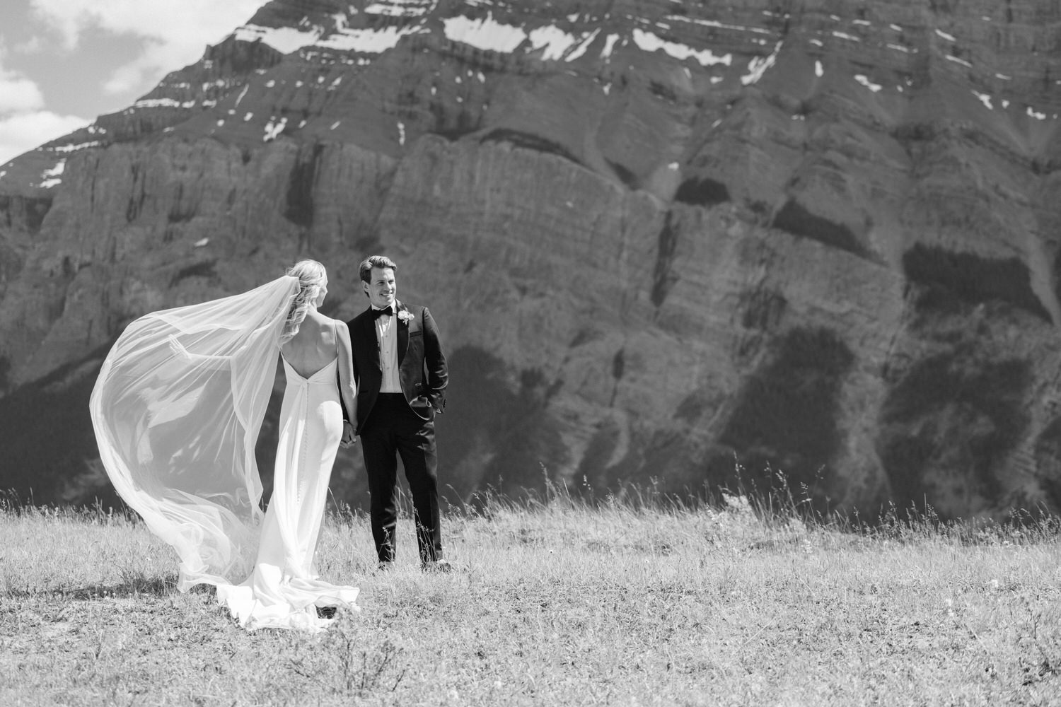 A black and white photo of a bride and groom walking together in a mountainous landscape