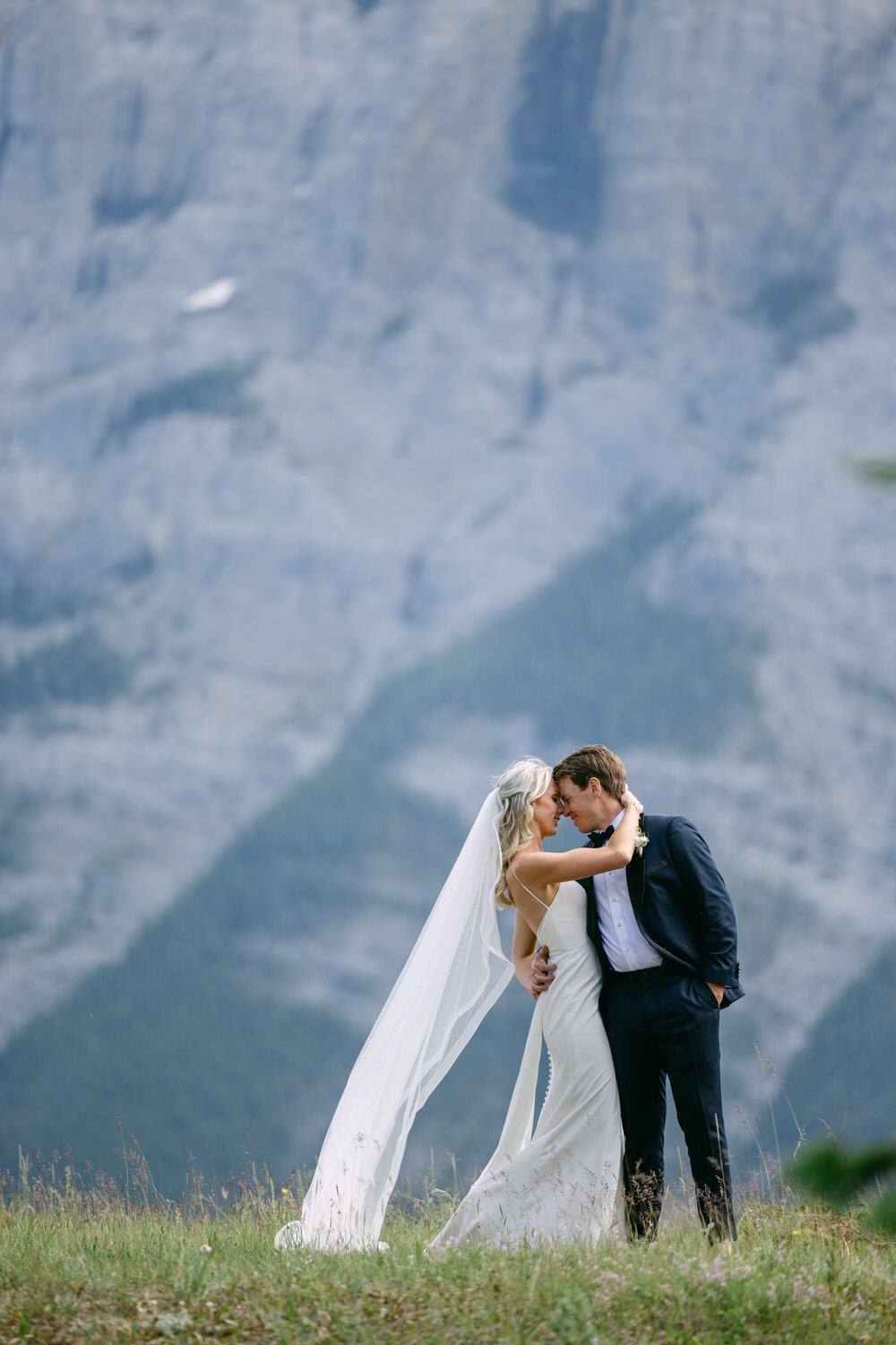 A bride and groom embracing with a majestic mountain backdrop.