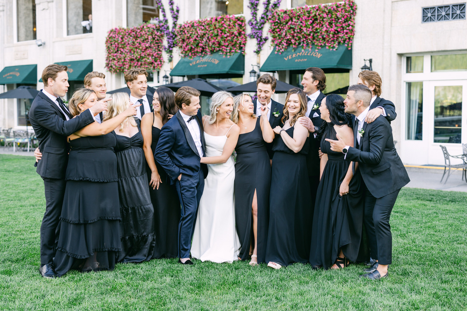 Group of people dressed in formal attire celebrating and posing together on a lawn with a building in the background