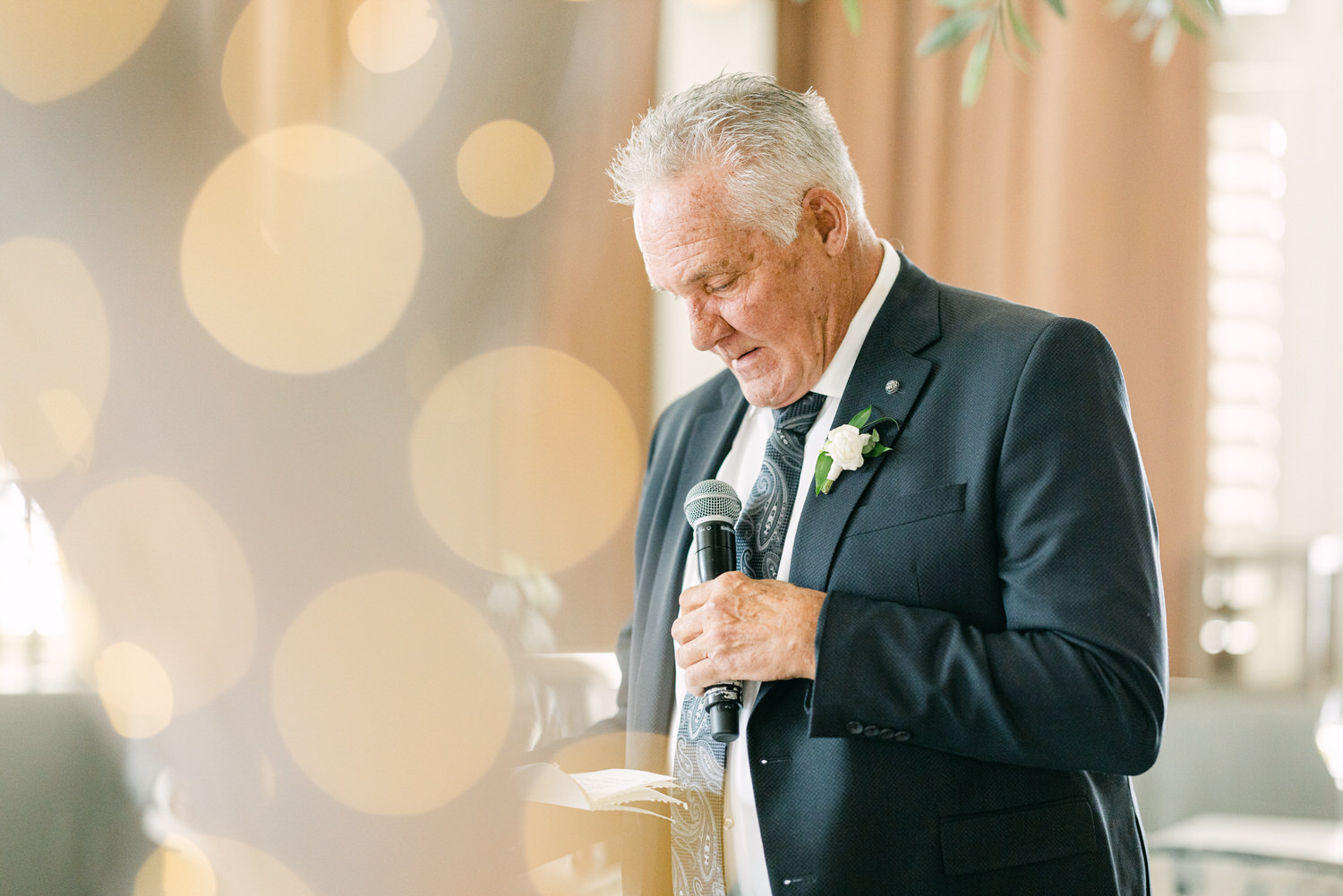 A man in a suit giving a heartfelt speech using a microphone, with bokeh lighting in the background.