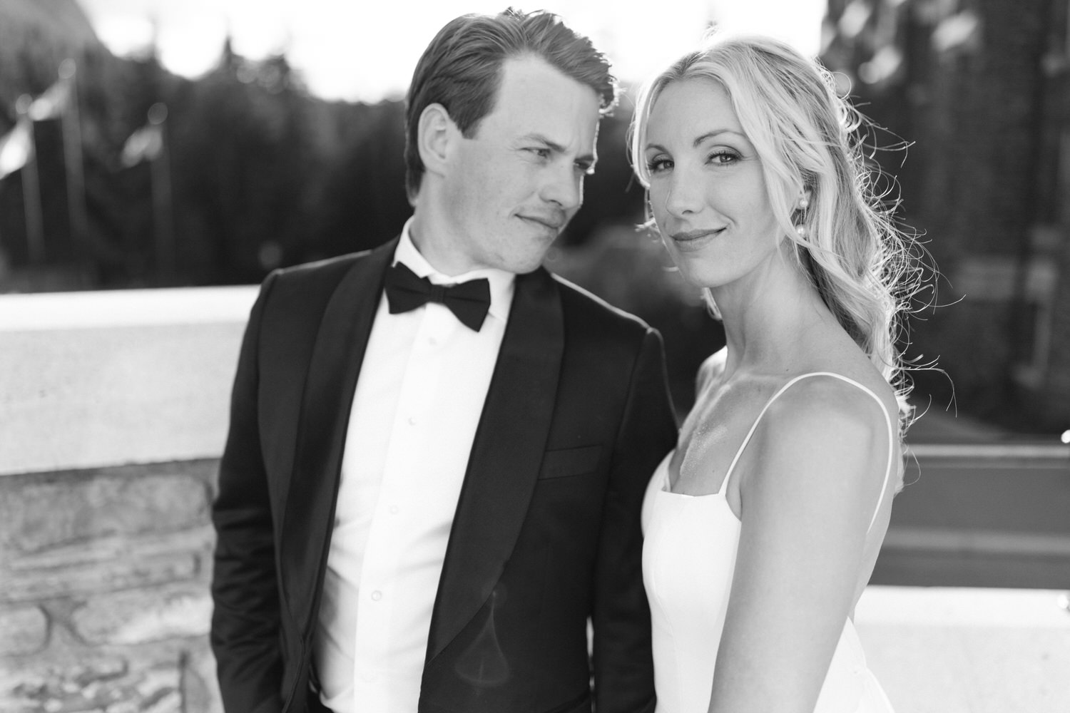 A man in a tuxedo and a woman in a white dress, both smiling, in a black and white photograph