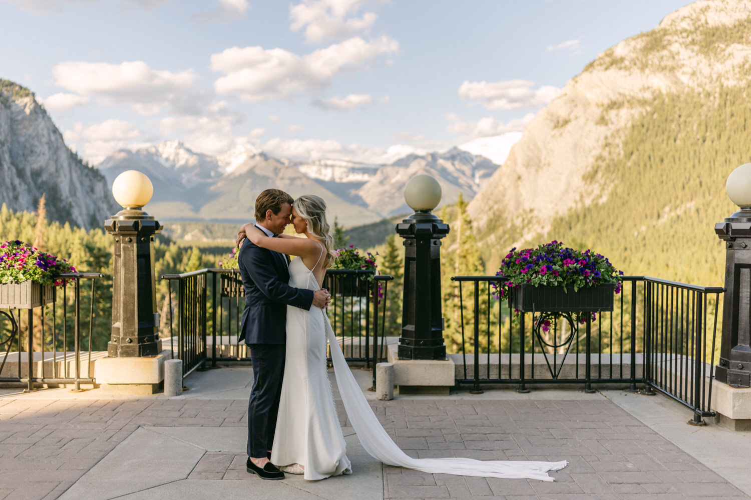 A bride and groom sharing an intimate embrace on a terrace with a breathtaking mountainous backdrop.