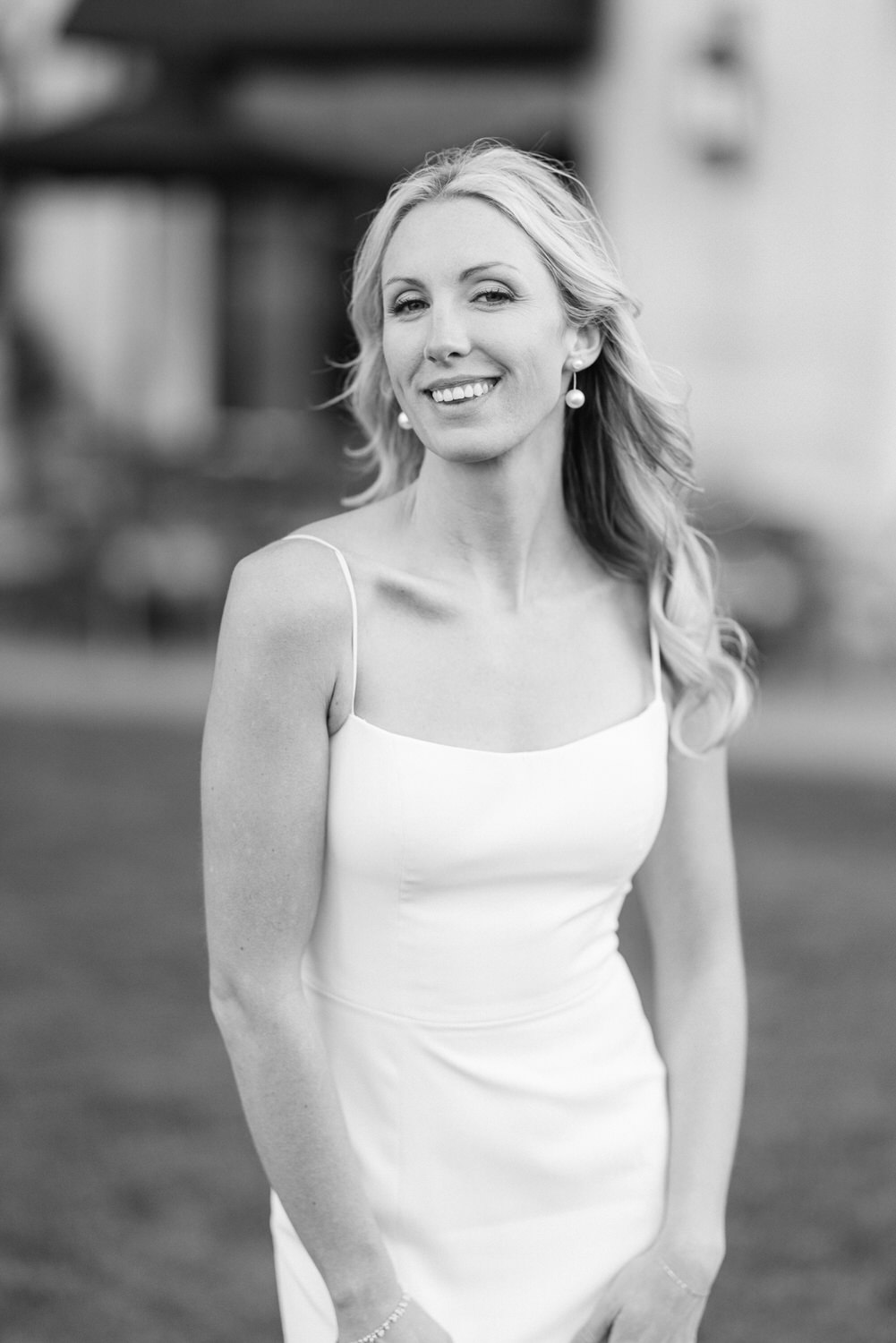 A black and white portrait of a smiling woman in an elegant sleeveless dress.