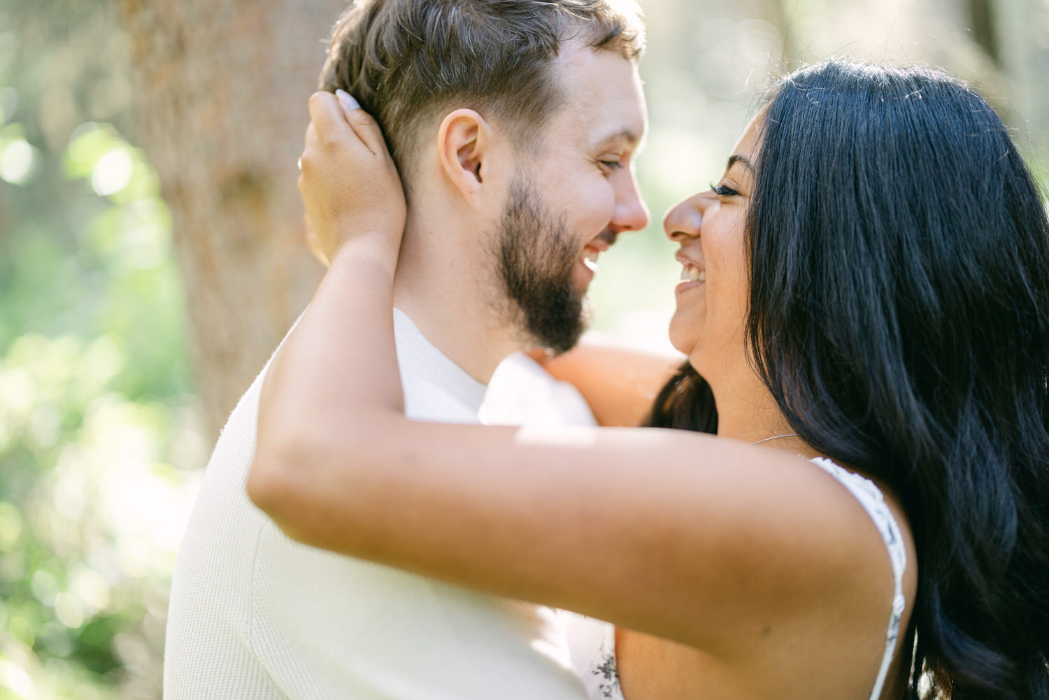 A man and woman smiling and embracing in a sunny, natural setting