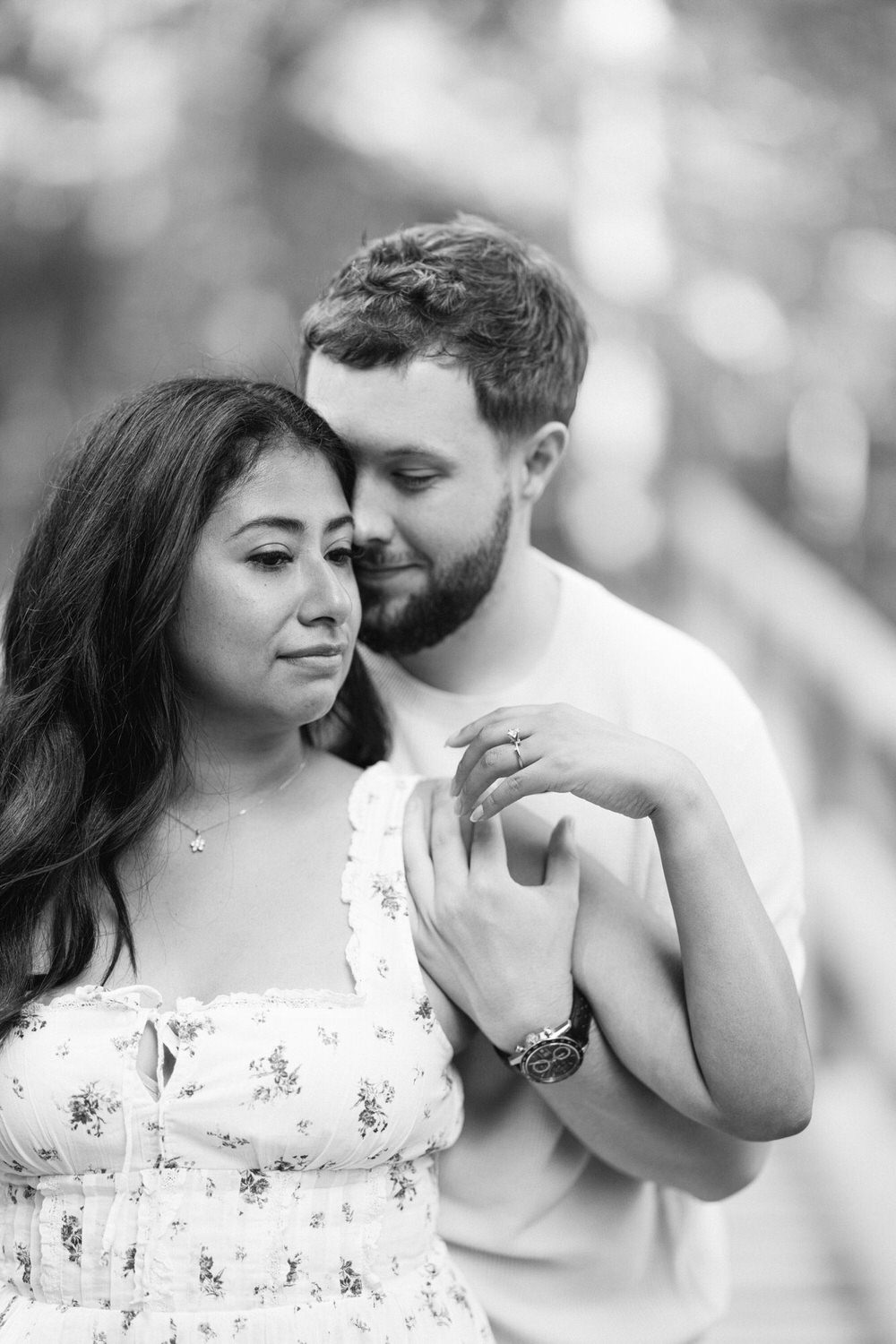 A black and white photo of a couple in a close embrace, with the man kissing the woman's forehead and the woman gazing thoughtfully into the distance.