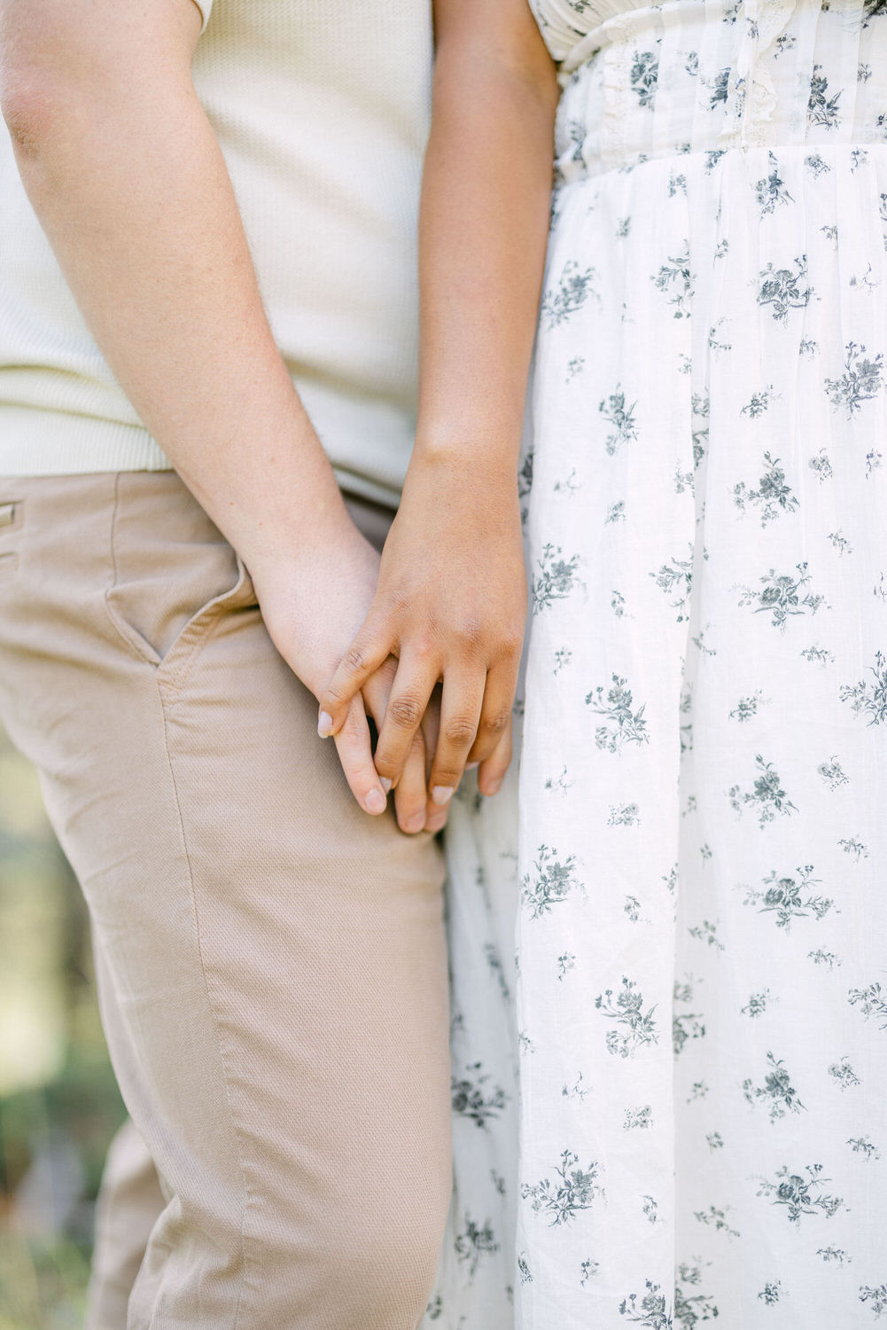 Close-up of a couple holding hands, focusing on the intertwined fingers against their neutral colored clothing.