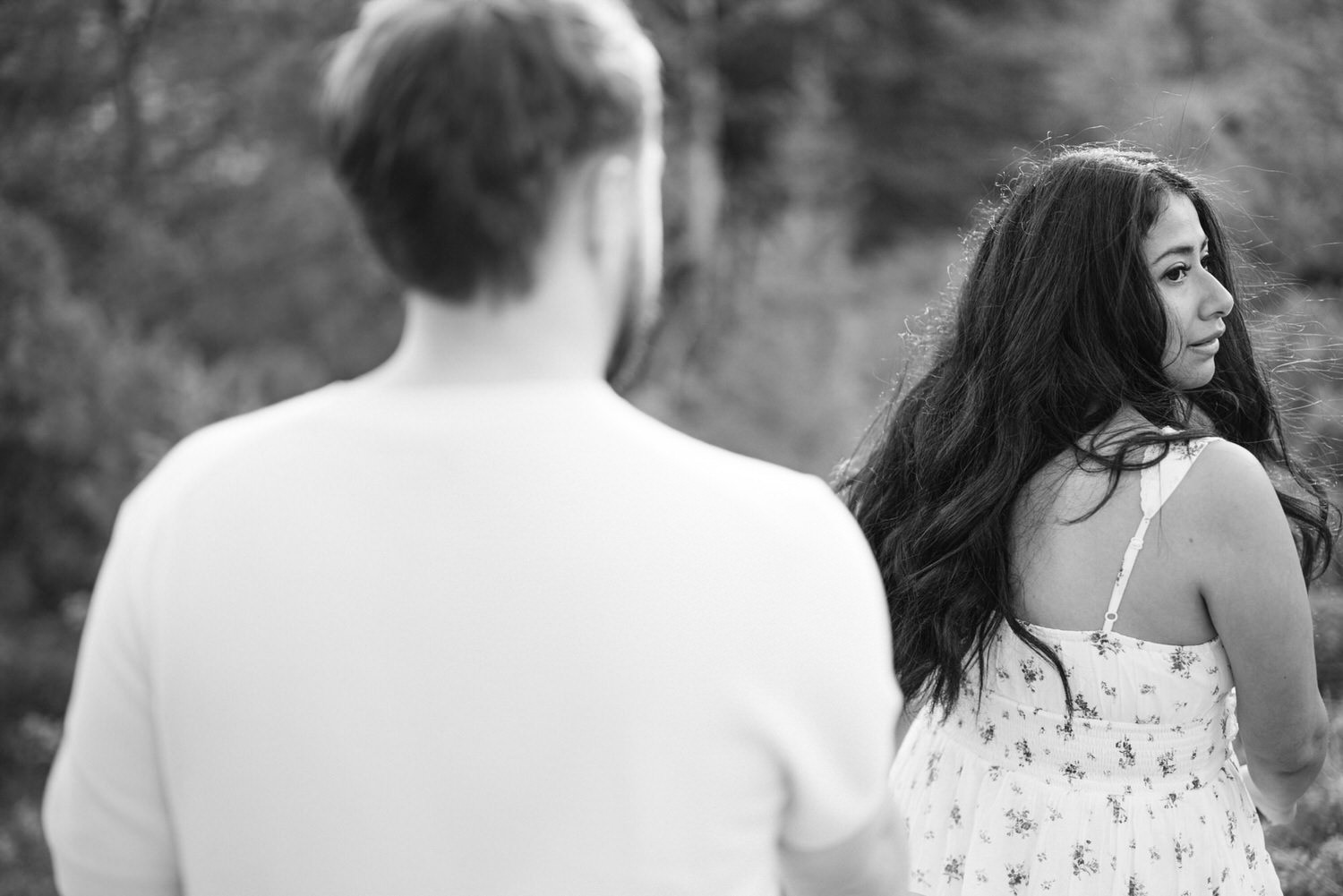 Black and white image of a woman glancing back over her shoulder at a man out of focus in the foreground.