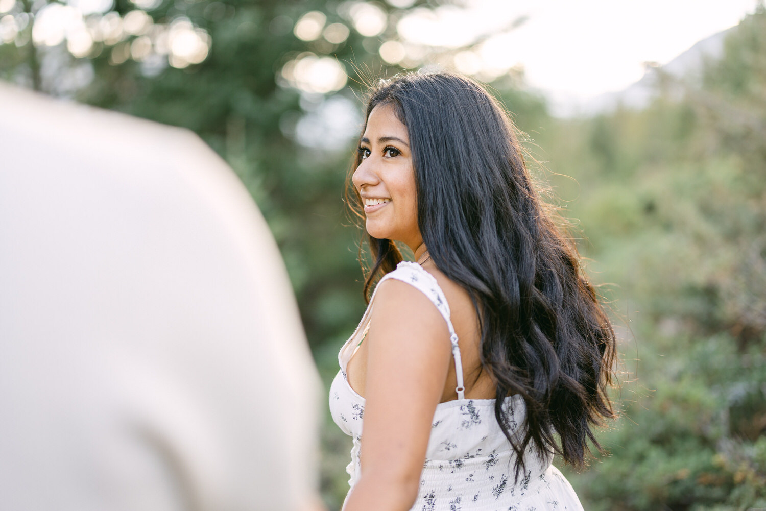 A smiling woman looking over her shoulder with lush greenery in the background.