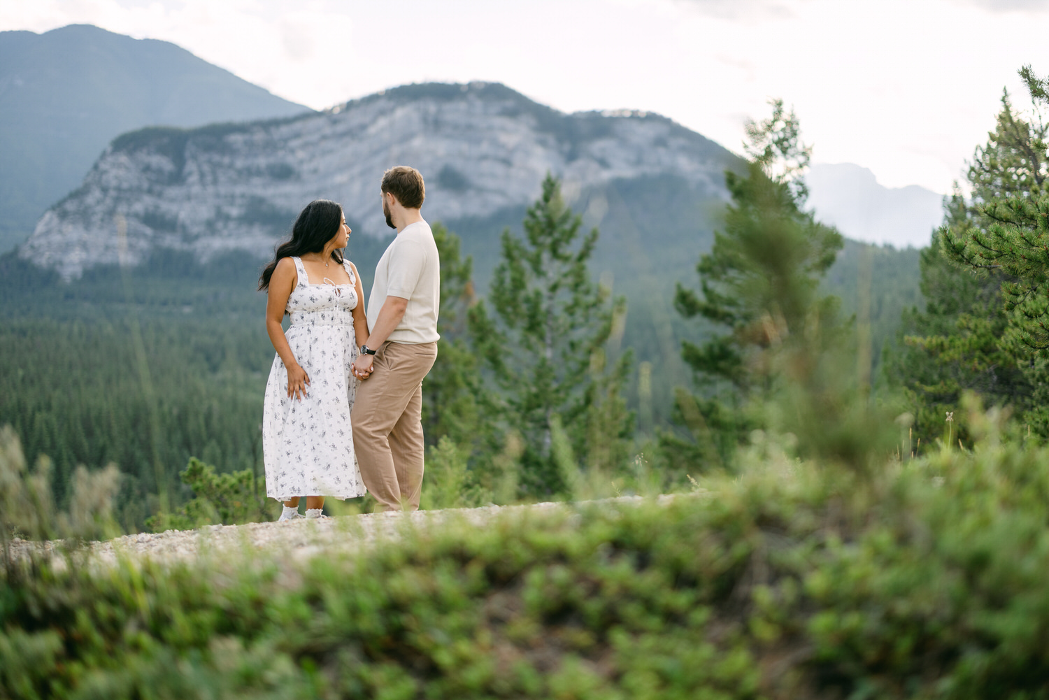 A couple holding hands and looking at each other with a mountainous backdrop.