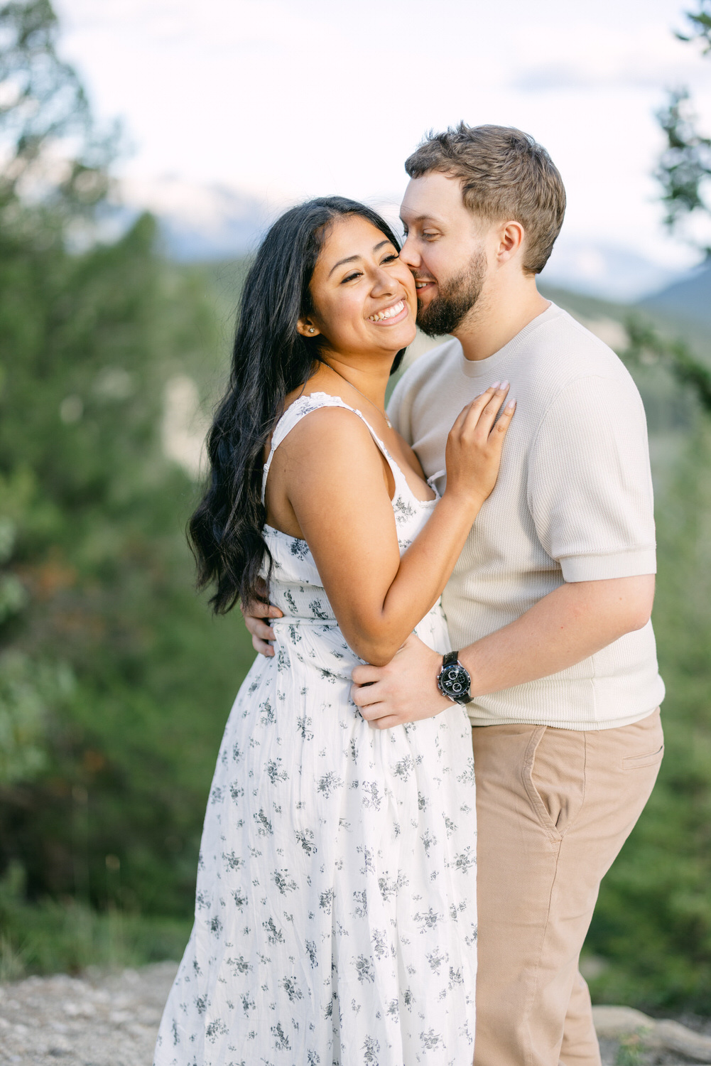 A man and woman sharing a tender embrace outdoors with a forest backdrop.