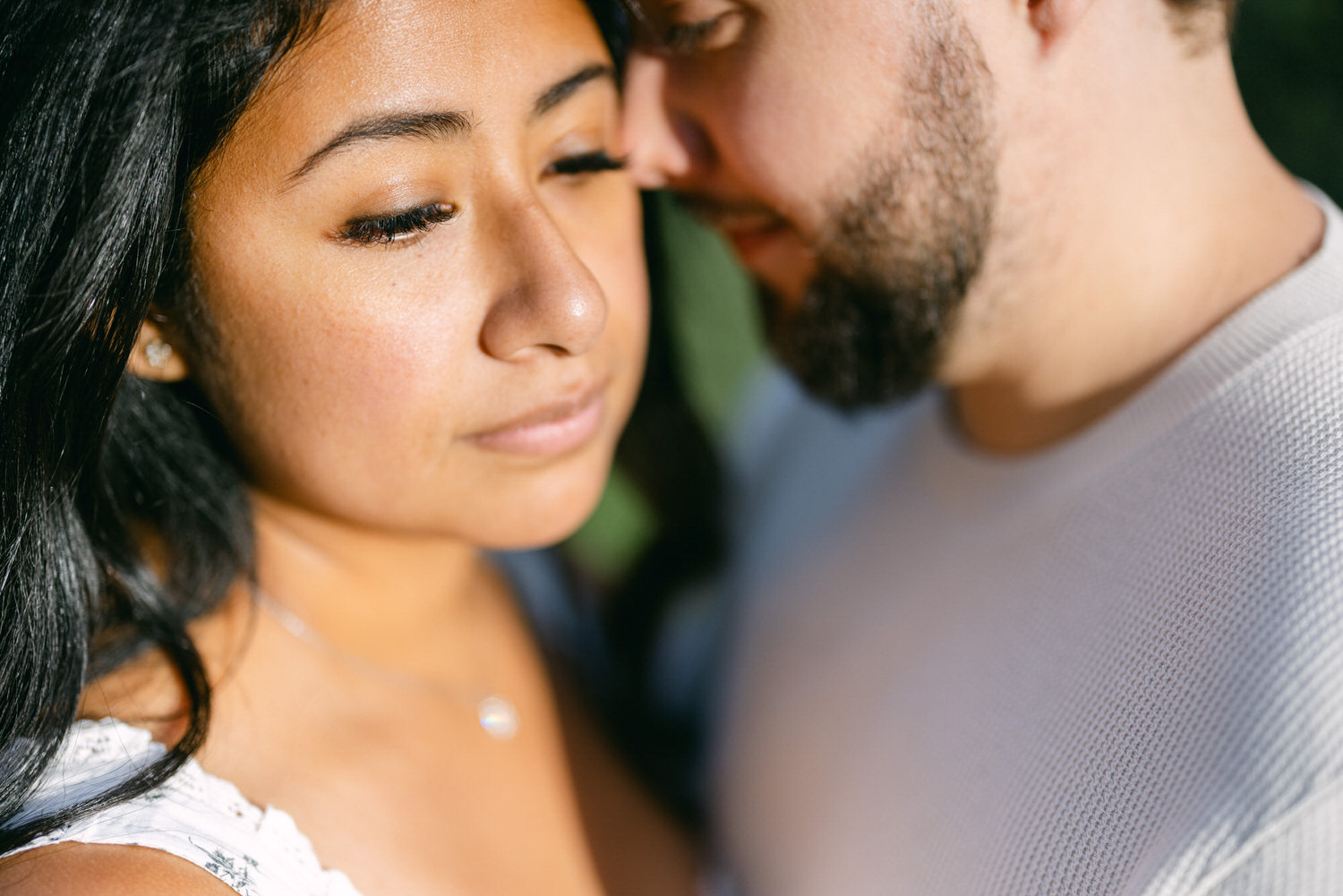 A close-up of a woman and a man in a tender and intimate pose, with soft focus and warm sunlight highlighting their faces.