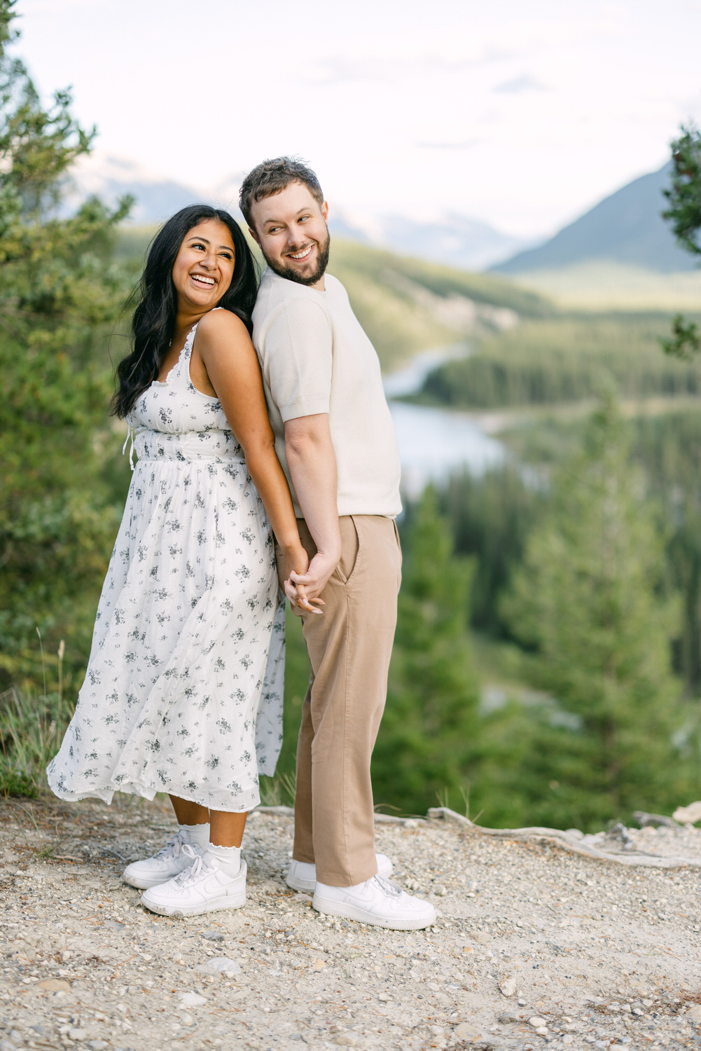 A smiling man and woman holding hands with a picturesque mountain landscape and river in the background.