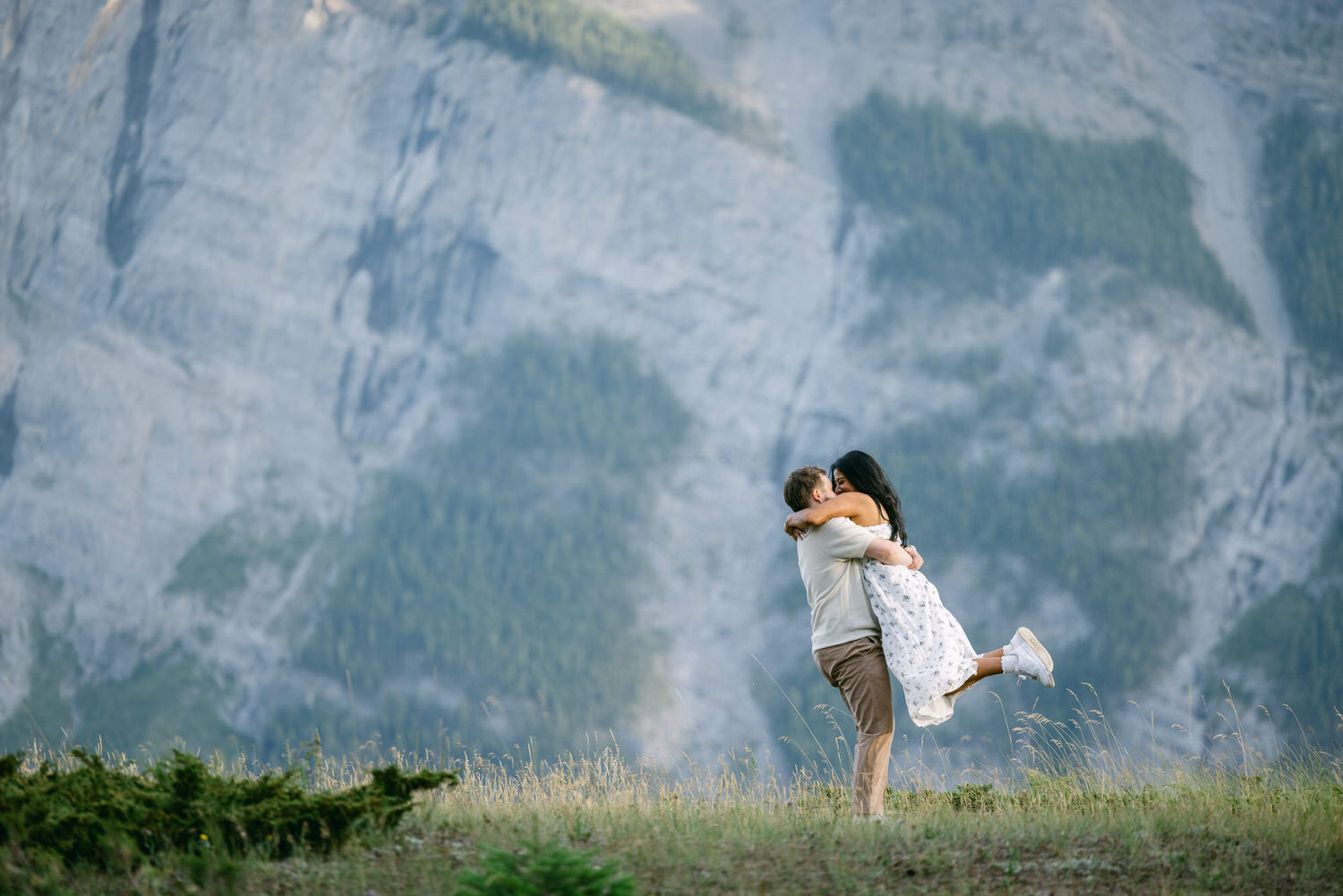 A couple hugging each other in a loving embrace with a scenic mountain backdrop.