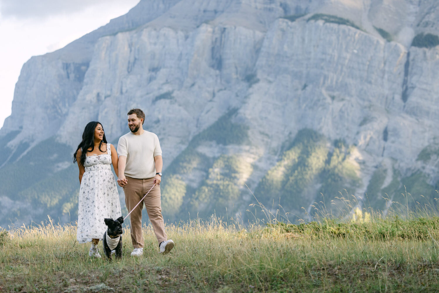 A couple walking their dog in a mountainous landscape.