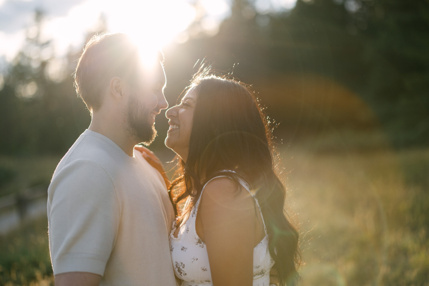 A couple standing close together in a sunlit field, sharing an intimate moment with a warm golden light surrounding them