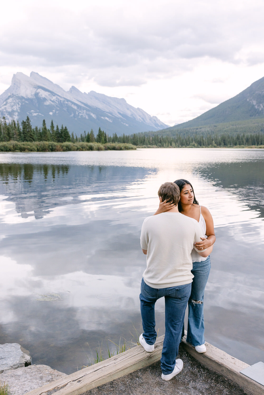 Two people sharing a moment by a calm lake with mountains in the background