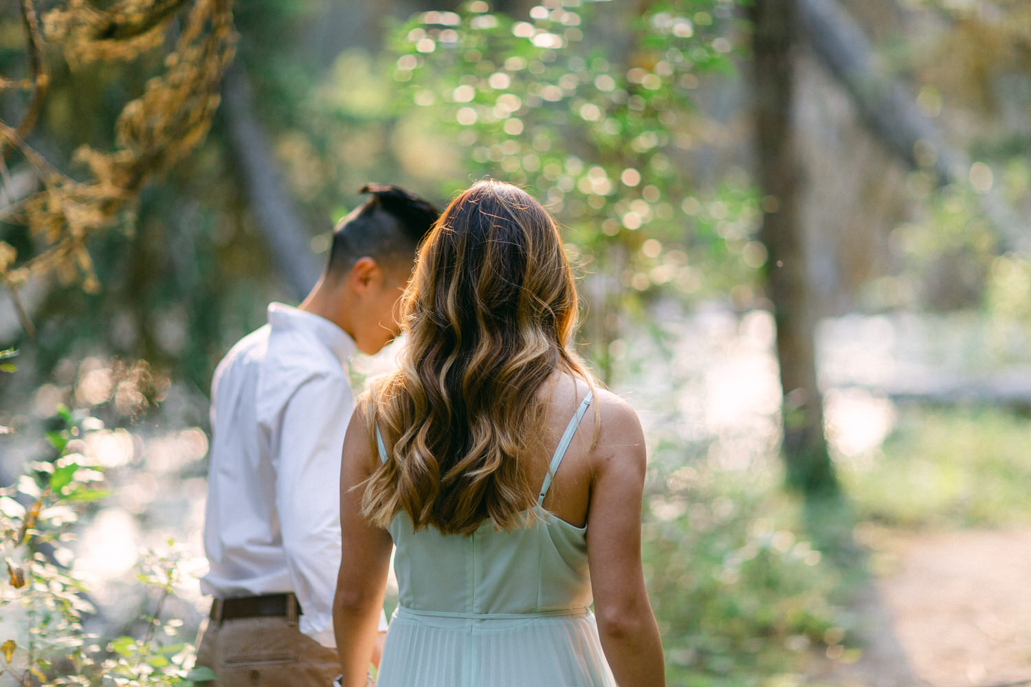 Two people walking away from the camera in a sunlit forest, suggesting a sense of companionship and tranquility.