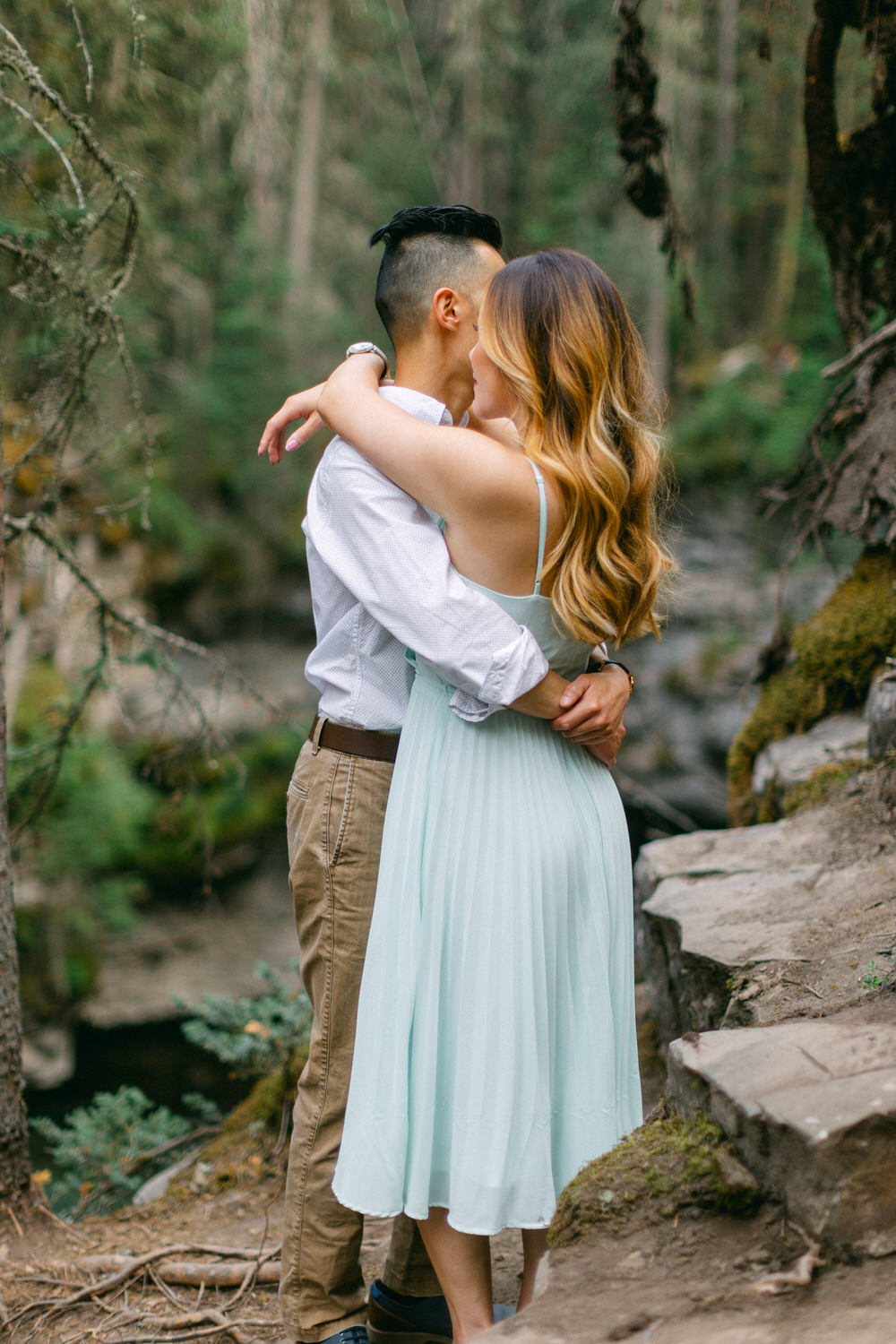 A couple shares a loving embrace amidst a wooded landscape, with the focus on their connection and the natural surroundings.