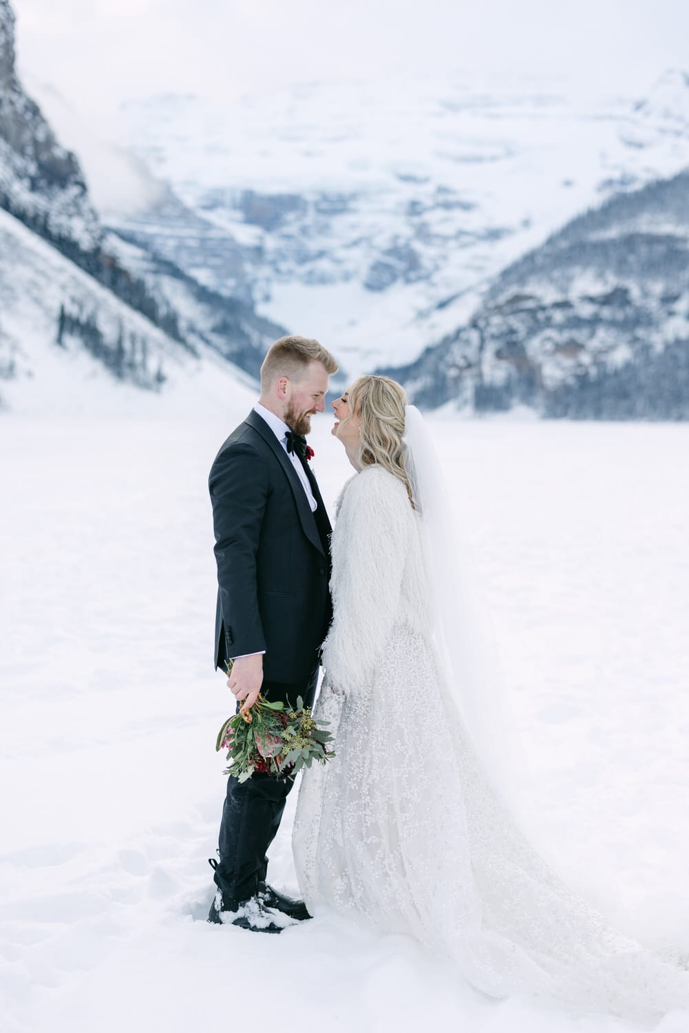 A bride and groom embracing in a snowy mountain setting